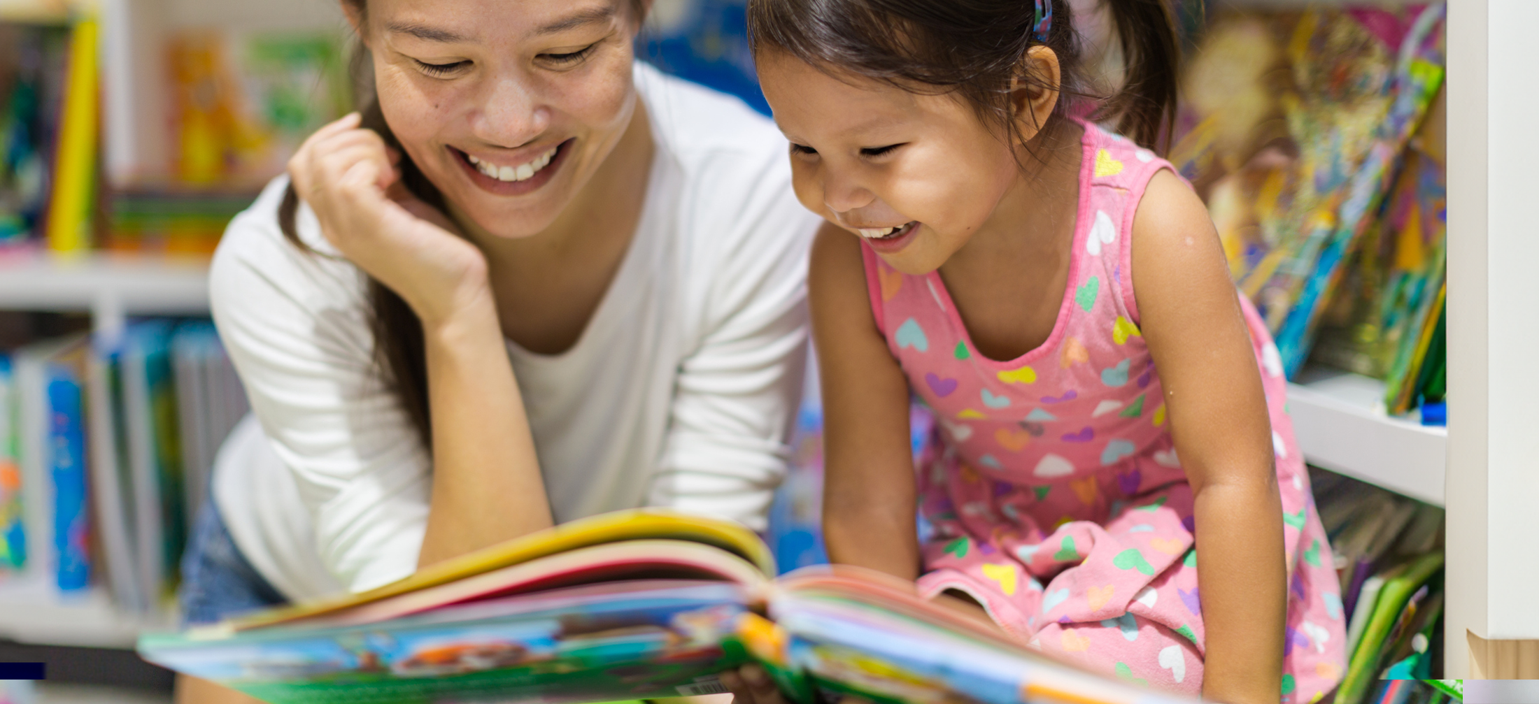 MOther and kindergarten age daughter smile as they read a big picture book