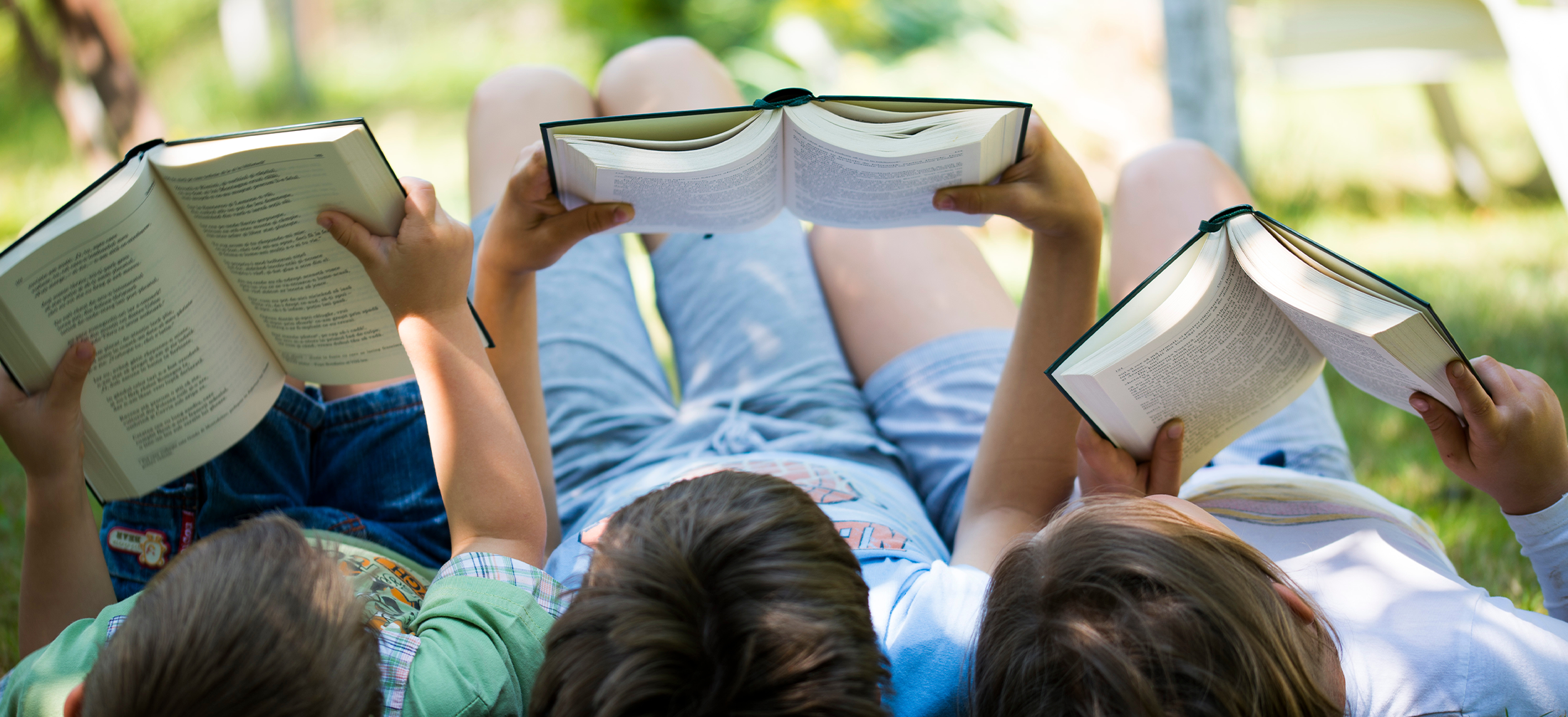 three children lying in the grass and reading books