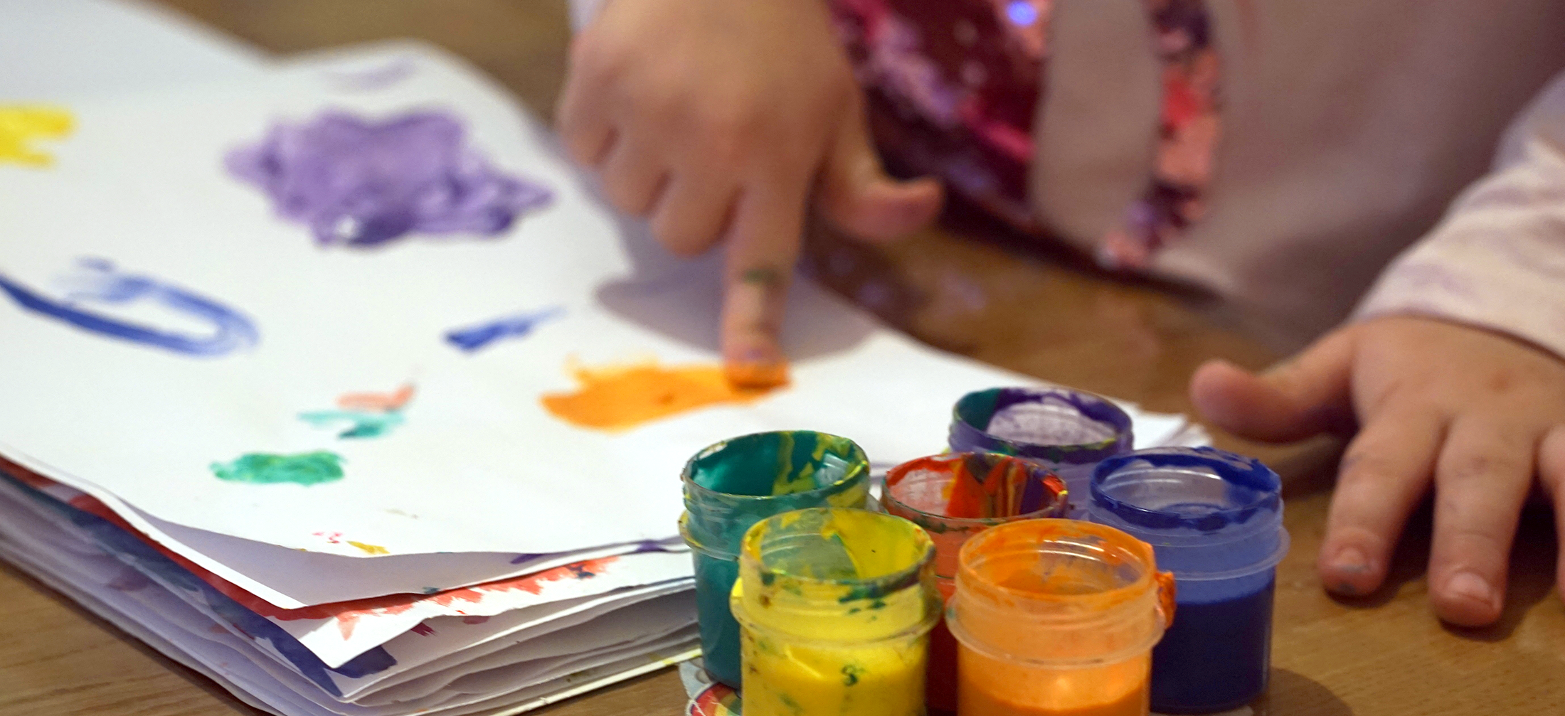 little finger using paints on paper with 6 color paint cups in the foreground
