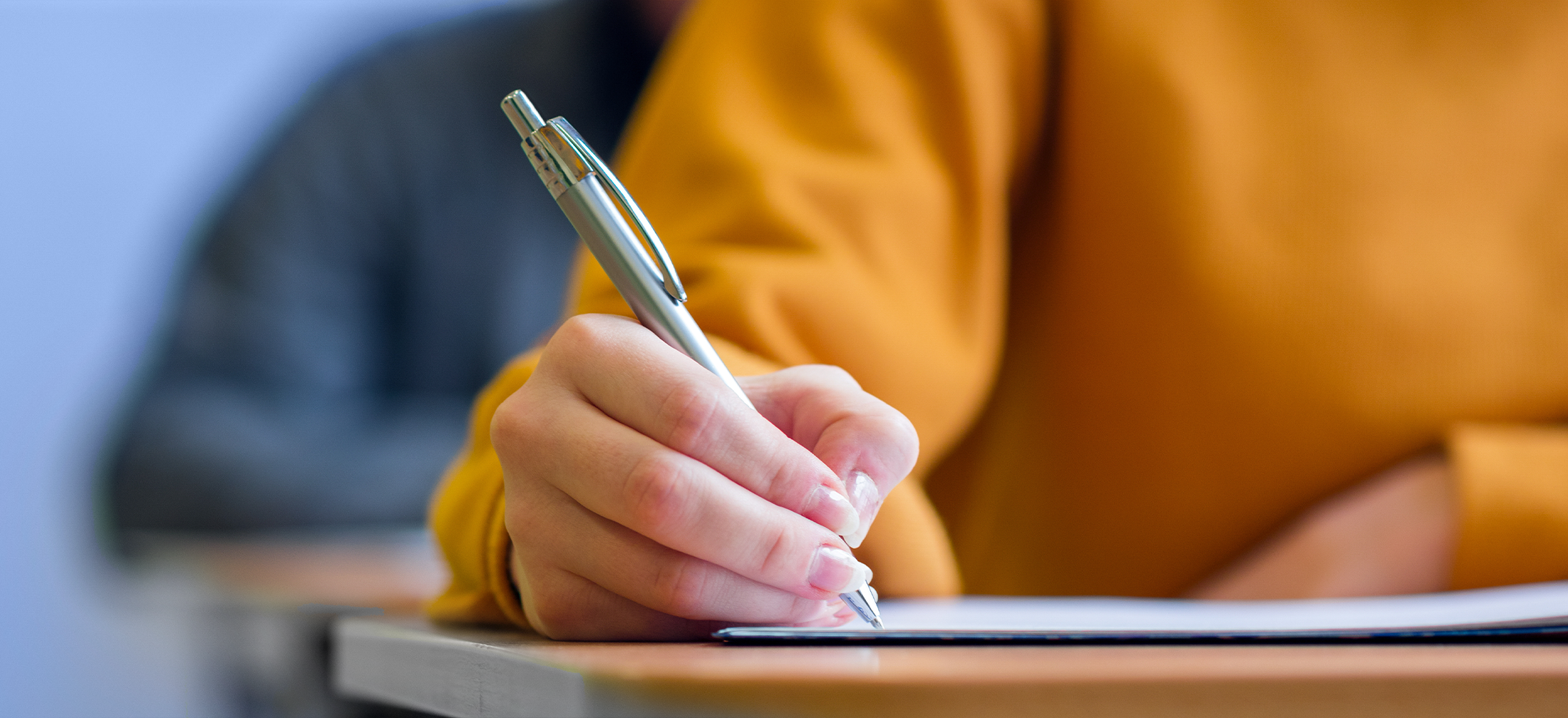 Students taking exam in classroom. Education test and literacy concept. Cropped shot, hand detail.