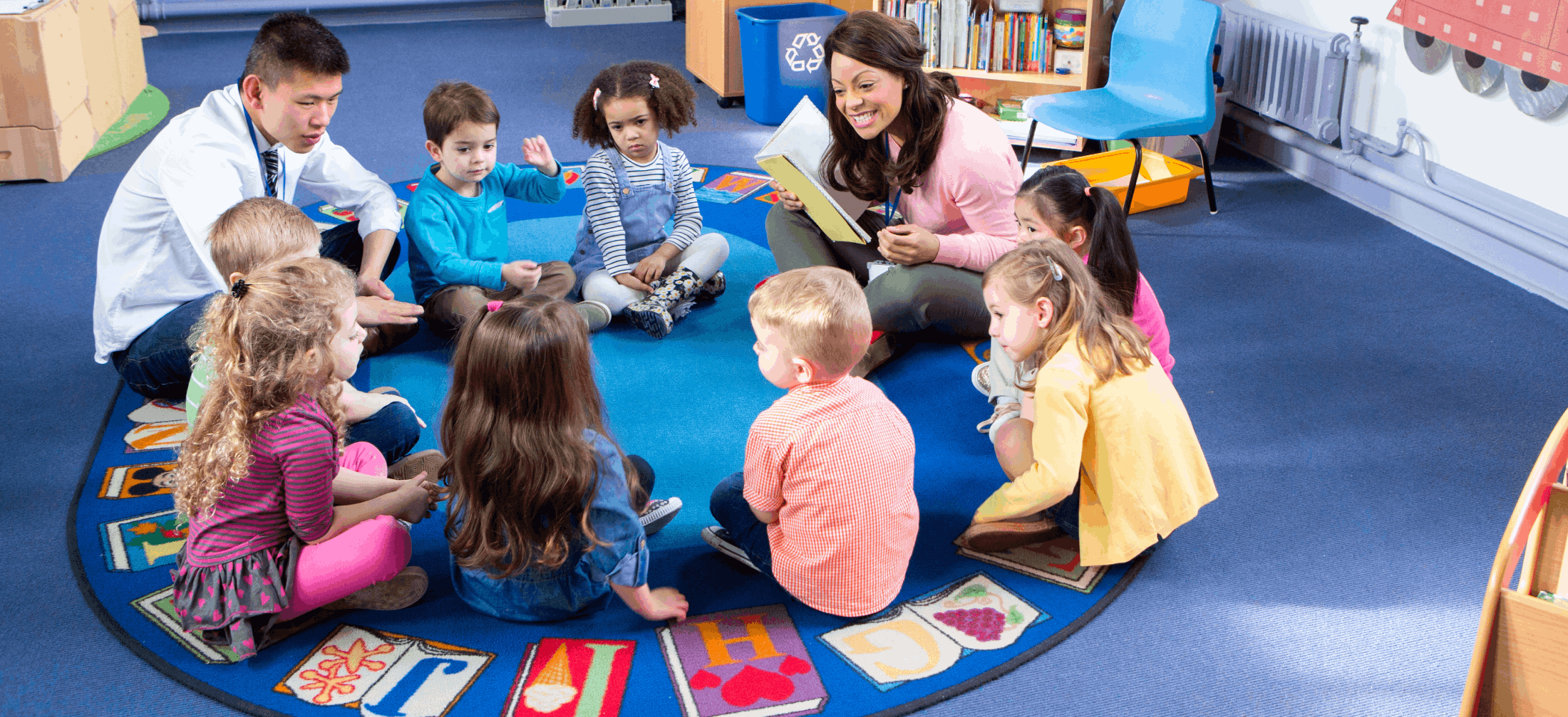 two early childhood educators work with children in a circle on a rug